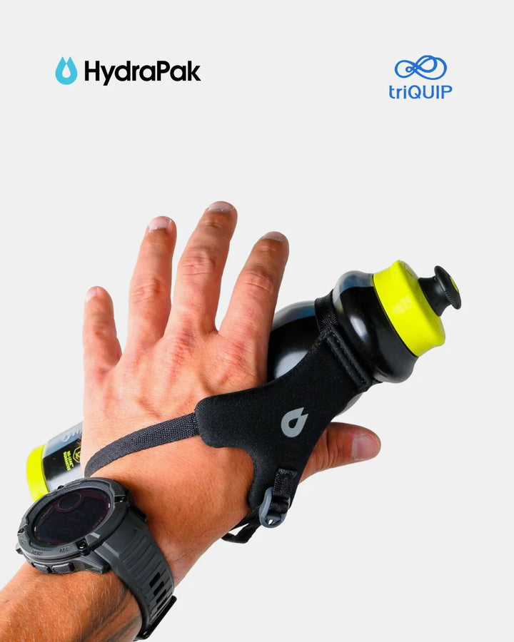 A hand wearing a black wrist strap that holds a black and neon yellow sports water bottle, with a black smartwatch on the wrist. The HydraPak logo is visible in the top left, and the triQUIP logo is visible in the top right, against a light gray background.