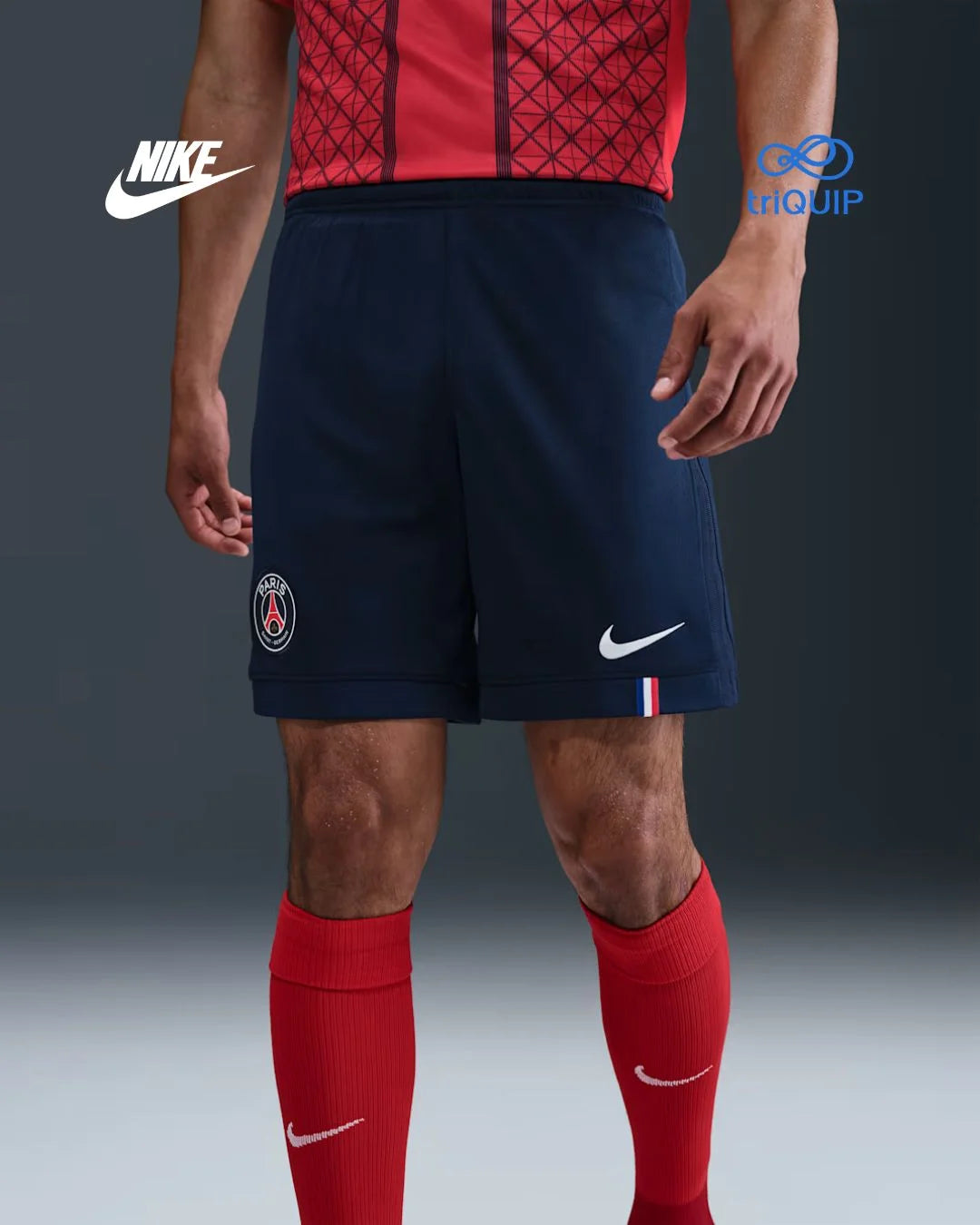A model wearing Paris Saint-Germain navy blue soccer shorts with a white Nike swoosh, red Nike socks, and a red patterned jersey top, shown from the waist down against a dark gray studio background with Nike and Equip logos.