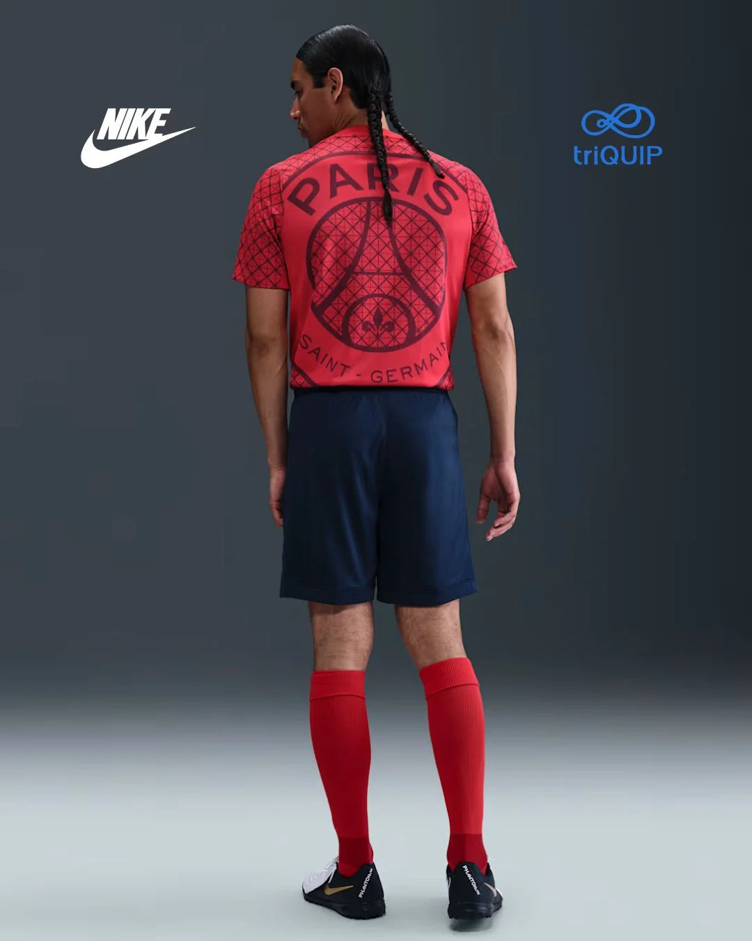 A model shown from the back wearing a red Nike Paris Saint-Germain jersey, navy shorts, and red socks, set against a dark gray studio background with Nike and triQUIP logos.